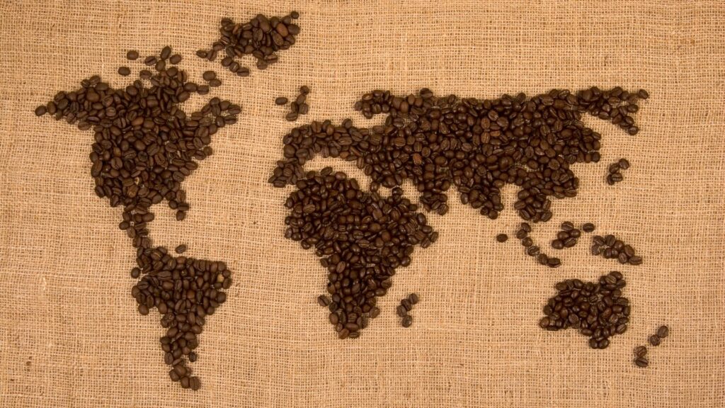 A flat lay image of a world map created from coffee beans on a burlap surface.