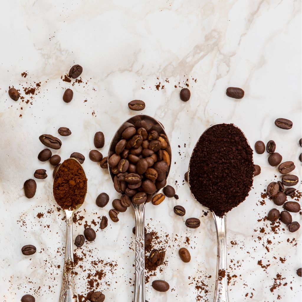 Three spoons of coffee—grounds, whole beans, and instant coffee—on a marble background.