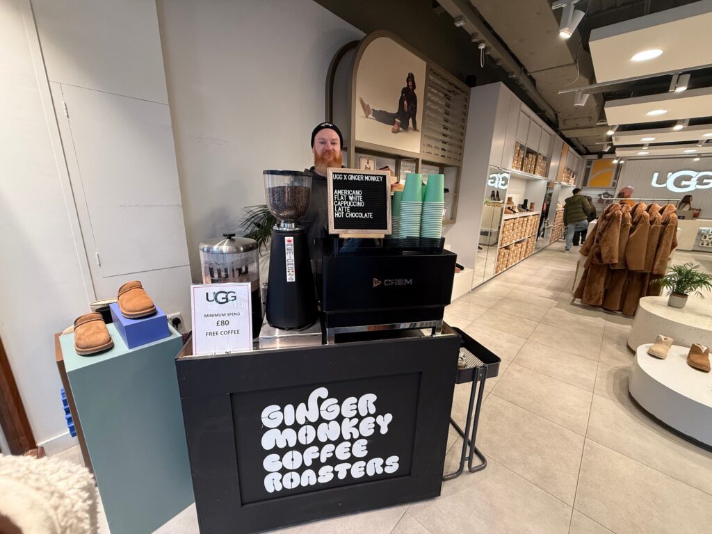 A barista standing behind a Ginger Monkey Coffee Roasters pop-up station inside an UGG store.