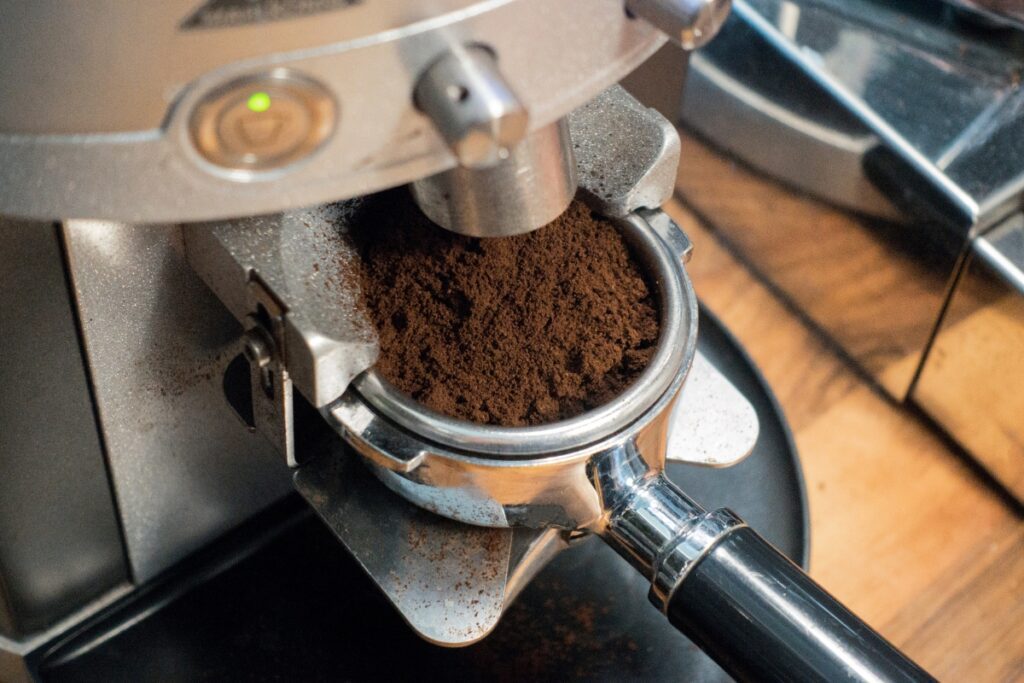 Close-up of freshly ground coffee filling up a metal portafilter basket directly from an espresso grinder nozzle.