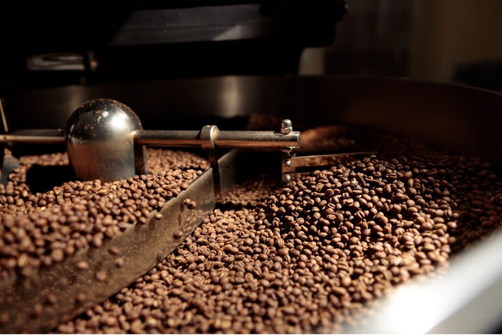 Freshly roasted coffee beans being stirred inside the cooling tray of a large commercial roaster.