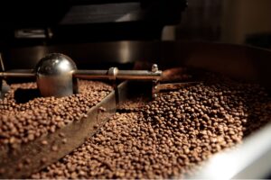 Freshly roasted coffee beans being stirred inside the cooling tray of a large commercial roaster.